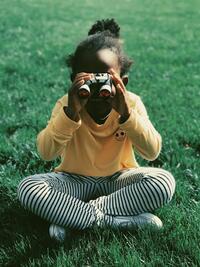 child sitting in the grass looking through binoculars