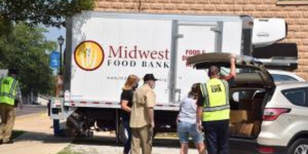 group of people loading boxes of food into a vehicle. Midwest Food Bank truck in background.