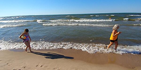 Child carrying beachball walking behind adult on Lake Michigan shore
