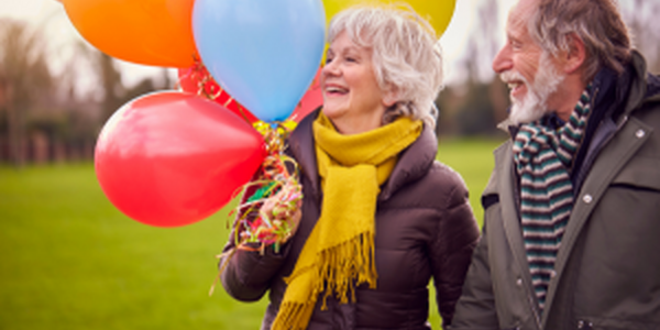older couple holding large bunch of colorful balloons