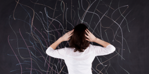 Woman with hands on either side of head staring at chalkboard full of chaotic lines
