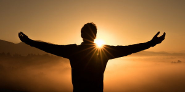 Man with widespread, open arms facing a bright sunrise