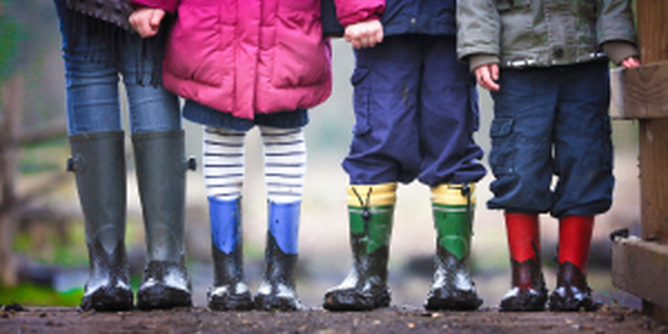Four young children wearing rain boots and holding hands outside