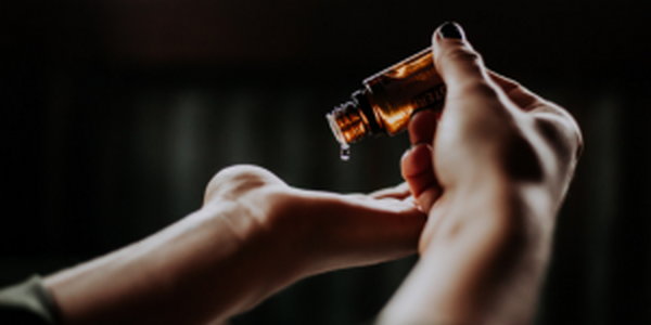 Person pouring massage oil from small glass bottle into opposite hand.