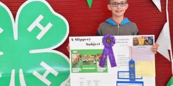 little boy holding 4-H project with blue ribbon and best of show ribbon