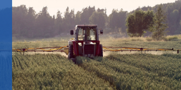 tractor with a sprayer spreading chemicals over a crop