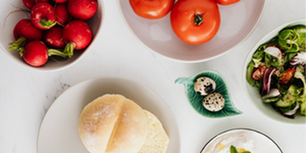 A bowl of tomatoes, strawberries, and cheese along with a plate of english muffins. 
