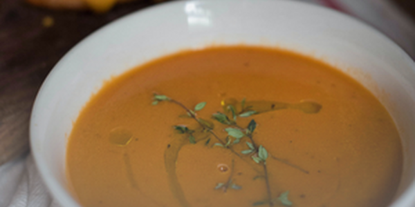 A round white bowl with a orange colored soup. 