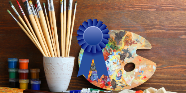 Art supplies on a table with a graphic of a blue ribbon over the top of the image.