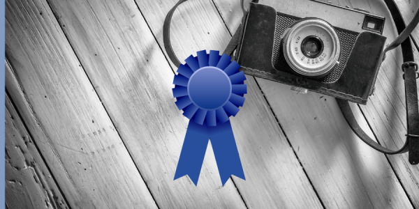 Camera laying on wooden pallet with a graphic of a blue ribbon over the image.