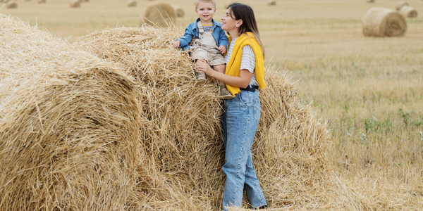 A woman holding her child who is sitting on a hay bale.