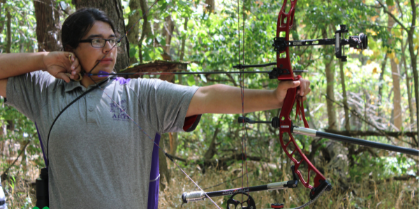 youth aiming a bow and arrow at a target