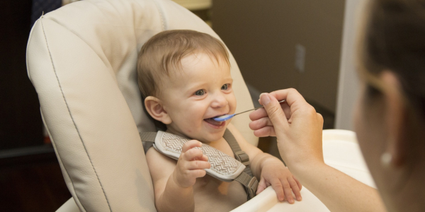 young child eating baby food in high chair.