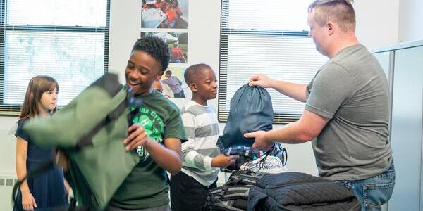 excited students receive backpack and supplies from older 4-H member
