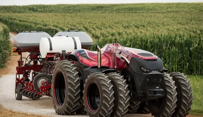 Red automated tractor driving through roadway near field.