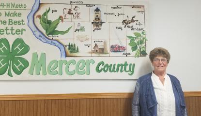 caucasian woman stands in front of map of Mercer County 4-H clubs 