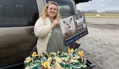 Woman outside holds sign in front of packets of frozen venison 