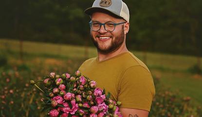 caucasian man in hat standing in field holding pink flowers 