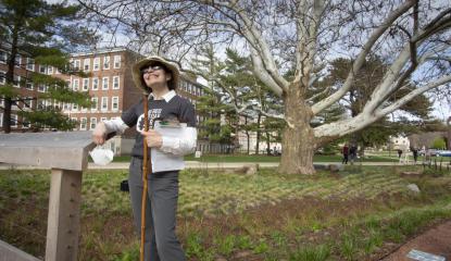 Woman in hat and sunglasses stands in rain garden 