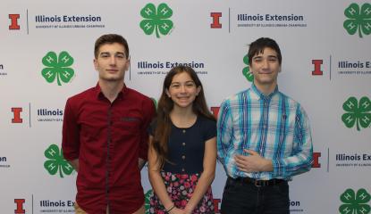 Simon, Olivia, & Jacob Truhlar stand in front of a step and repeat banner with the Extension & 4-H logos