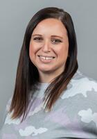 Headshot photo of Courtney. She is wearing a gray and purple shirt and is in front of a gray background