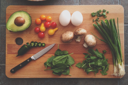 Cutting board with avocado, jalapeno, tomatoes, eggs, mushrooms, basil, and green pepper.